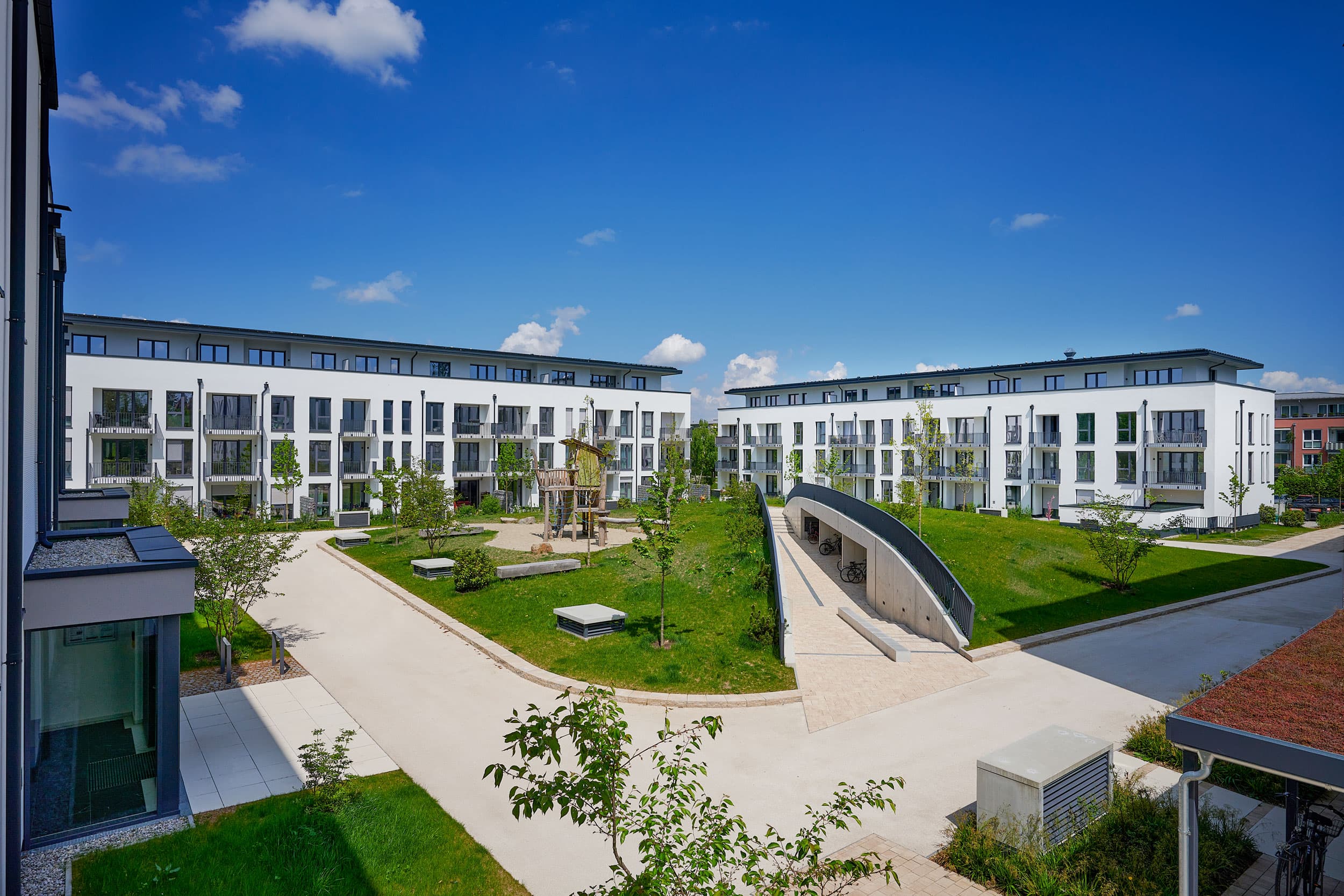 Begrünter Innenhof des Annelies Quartiers in Haar bei München mit Spielplatz, Wohngebäuden und Rampe zur Tiefgarage