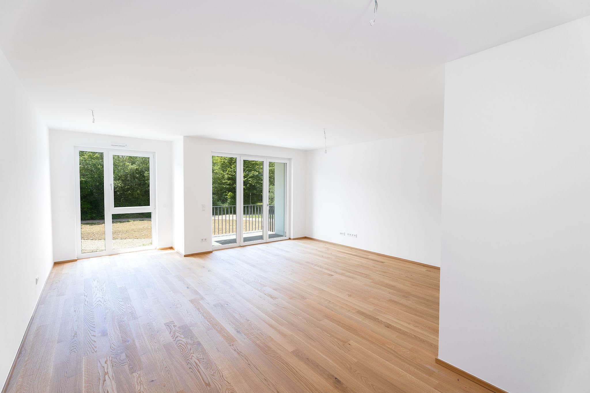 Leerer Wohnraum im Annelies Quartier mit Eichenparkett und zwei Fenstertüren zum Freibereich