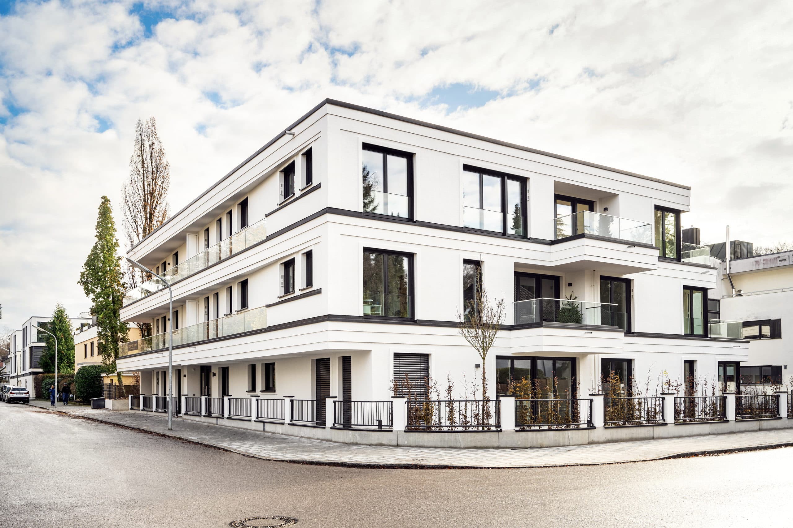 Das fertiggestellte Wohnjuwel an der Menterschwaige als Eckhaus in München-Harlaching, weiße Fassade mit umlaufenden Gesimsbändern
