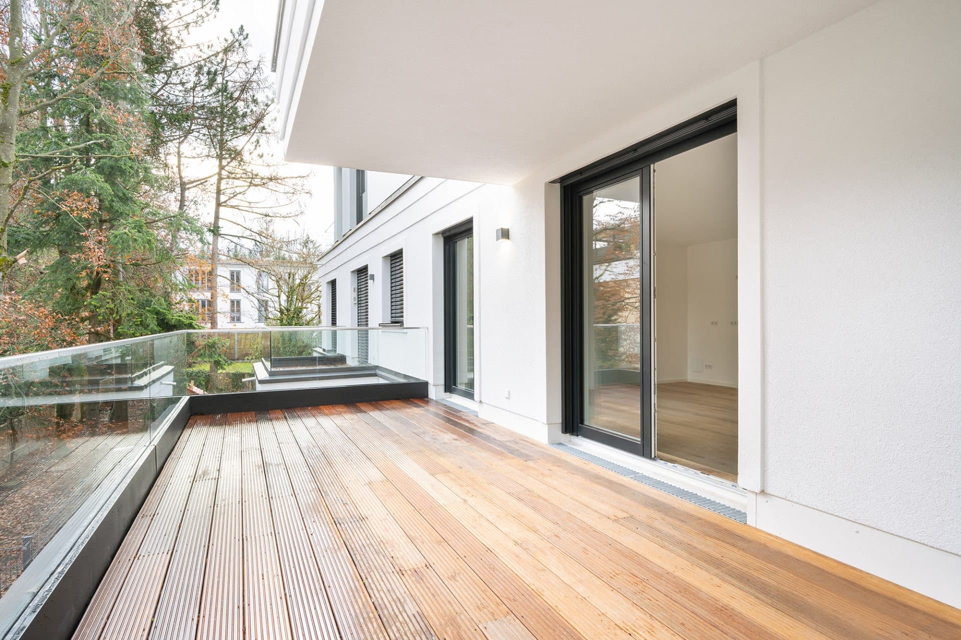 Terrasse im Wohnjuwel an der Menterschwaige mit Holzdeck, Glasbrüstung und Blick in die begrünte Nachbarschaft